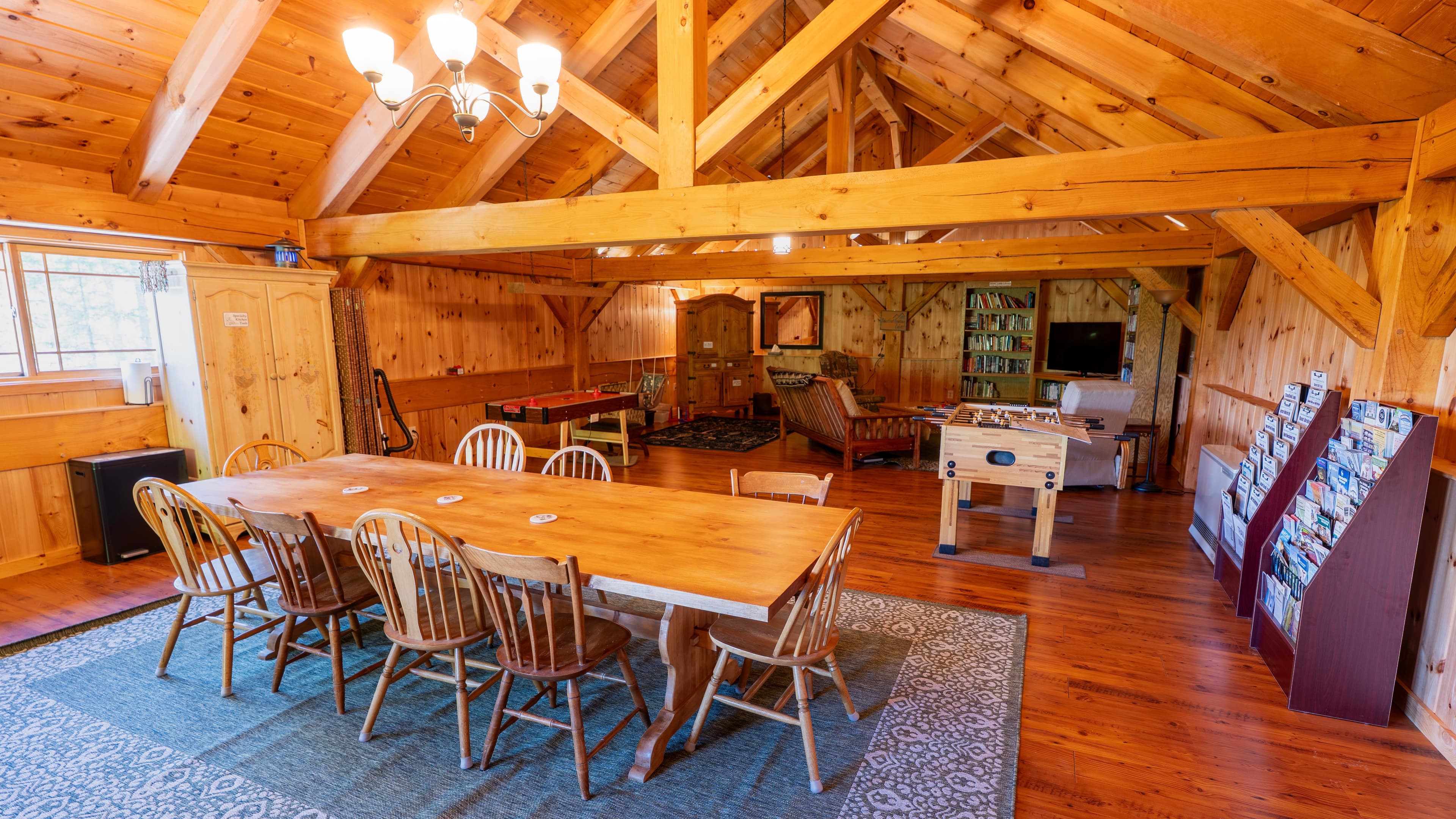 A spacious wooden dining area with a large table, chairs, and recreational space in a rustic cabin setting.