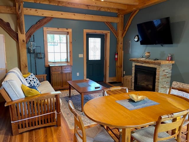 Cozy living room with wooden beams, a fireplace, a round dining table, and a green door.