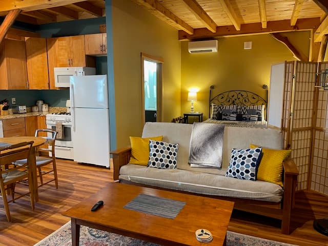 Cozy living space featuring a sofa, coffee table, and kitchen area with wooden beams above.