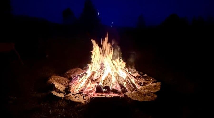 A vivid bonfire crackles against a dark blue evening sky.