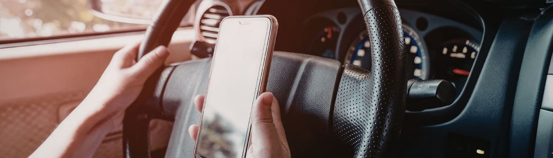 A person holding a smartphone while gripping the steering wheel of a car.