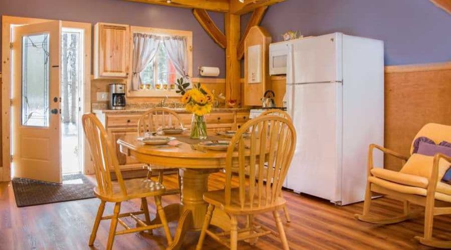 Cozy kitchen with wooden dining table, white appliances, and an open door leading outside.