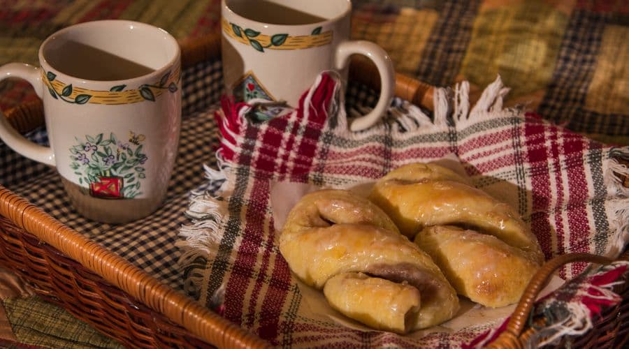 A basket with pastries and two mugs on a patterned tablecloth.