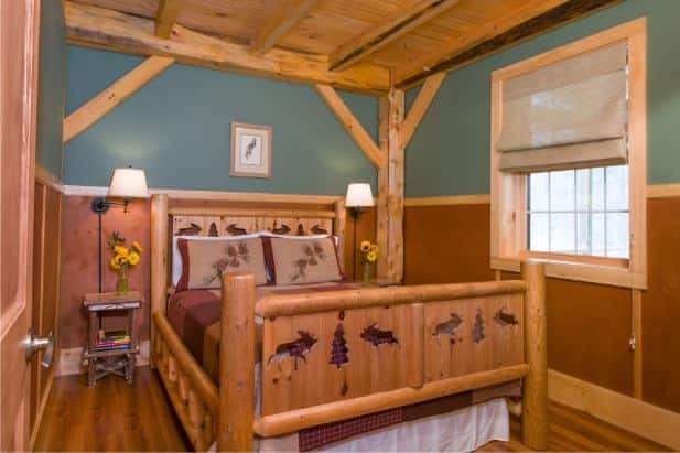 Owl's Branch guest room with rustic wood carved bed, two nightstands with lamps, wood floor and window with shade